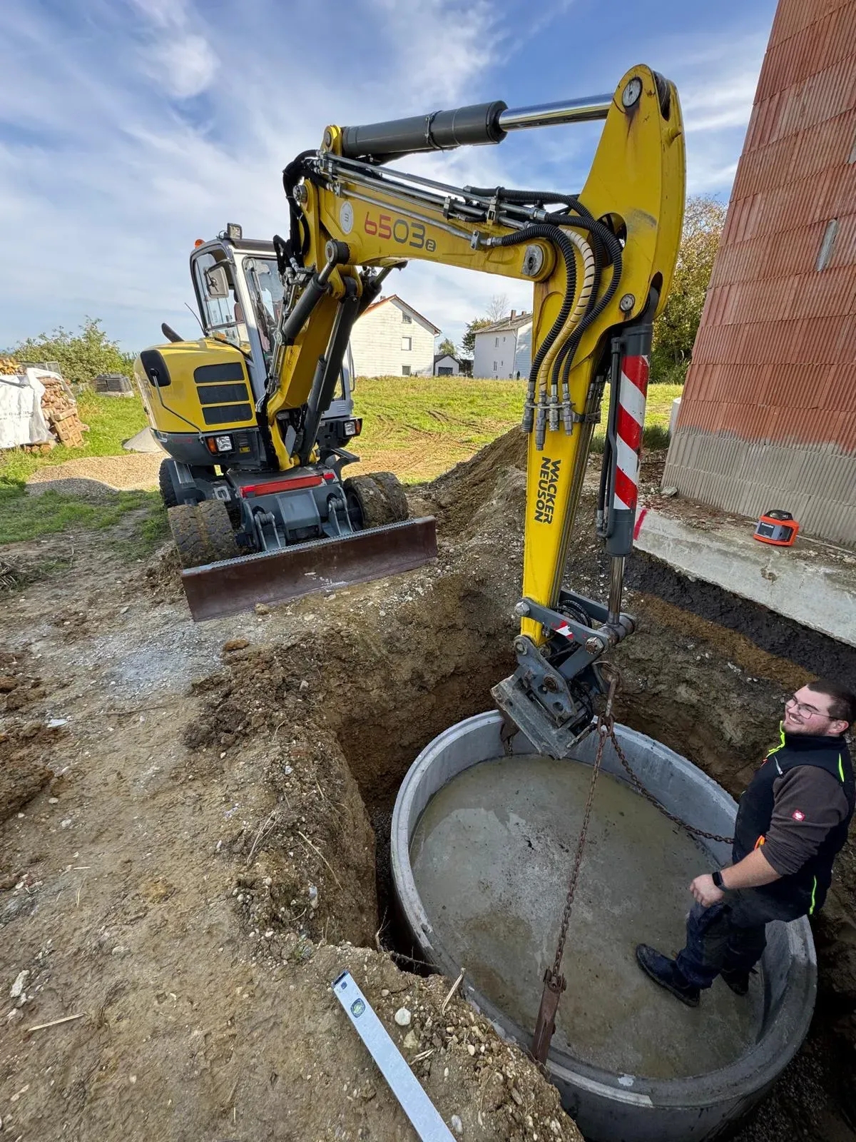Bagger setzt eine Regenwasserzisterne in die ausgehobene Baugrube